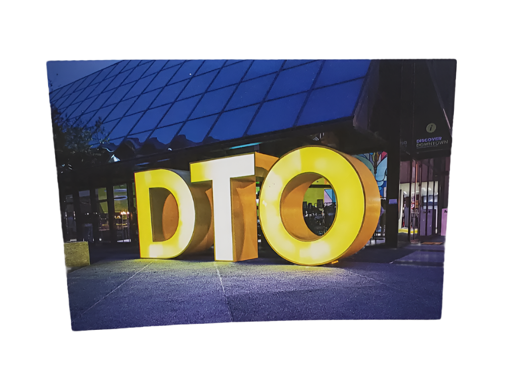 Large illuminated letters 'DTO' in front of a building at night.