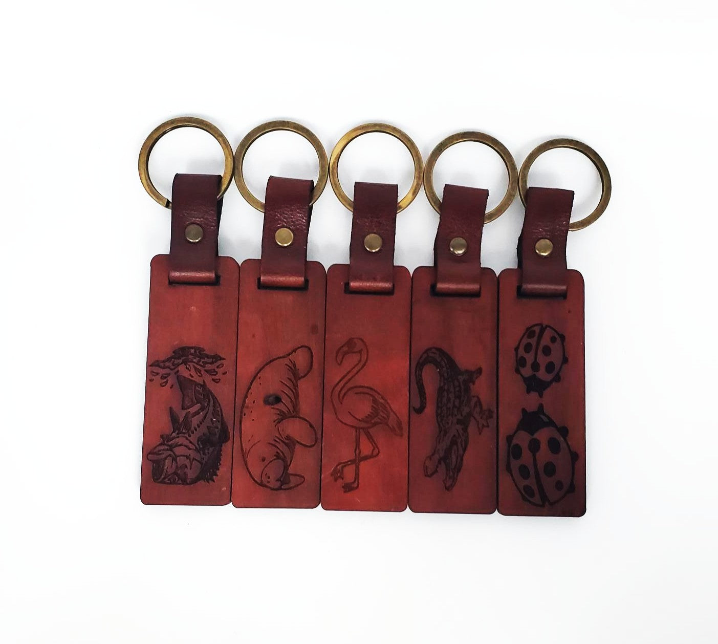 Five wood keychains with embossed designs on a white background