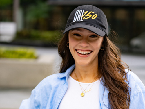 Woman wearing a cap with 'ORL 150' text, smiling outdoors