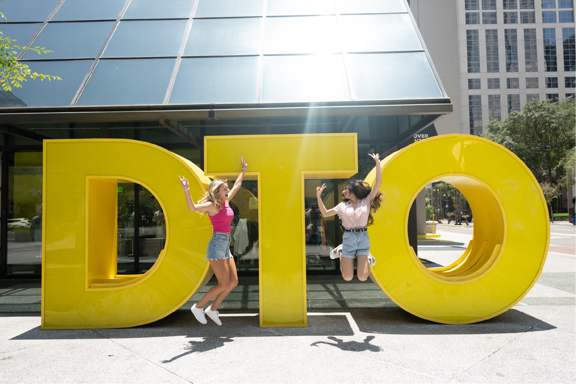 Two people posing behind large yellow letters spelling 'DTO' in an urban setting